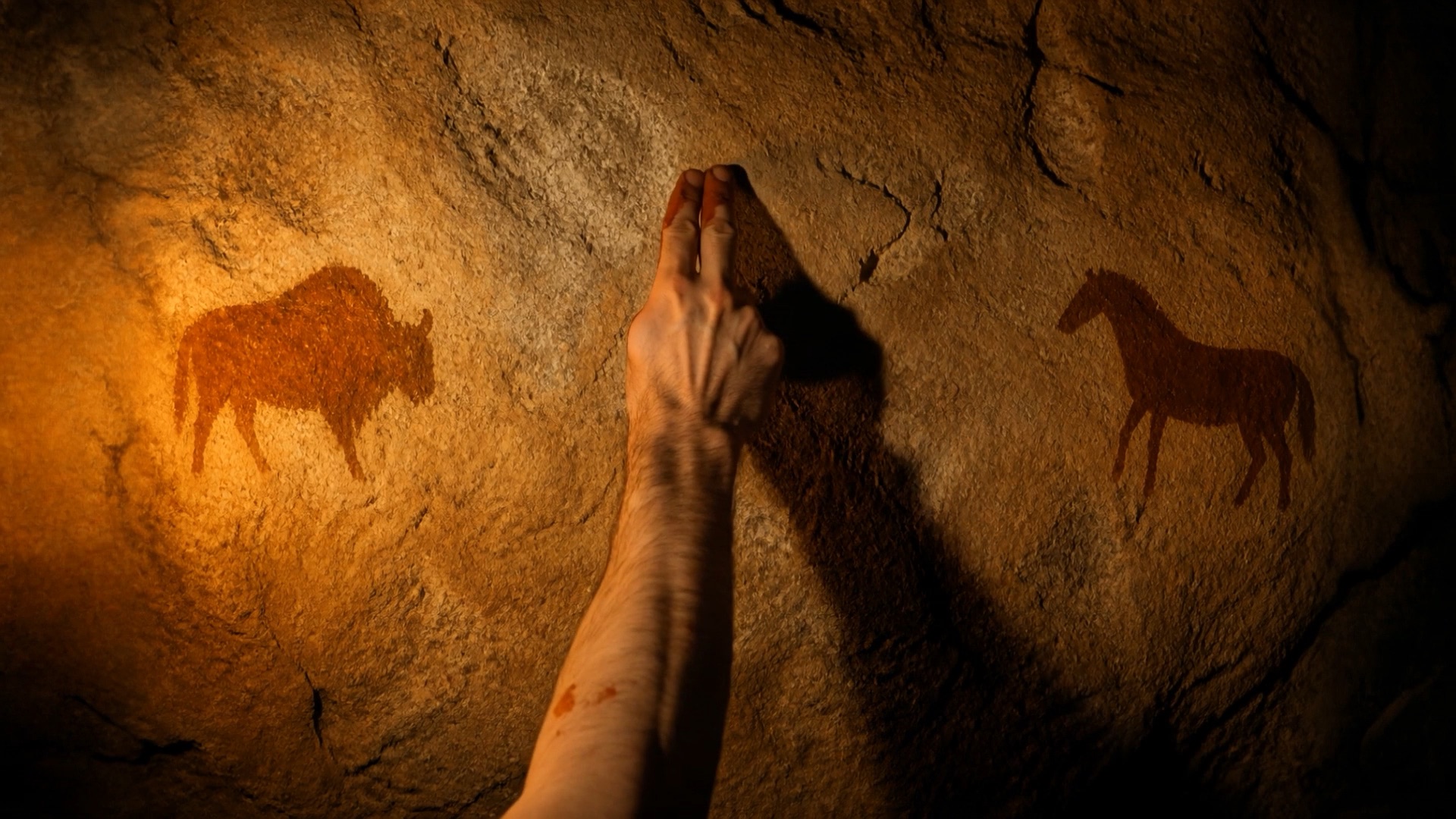 A hand painting a red circle on a cave wall